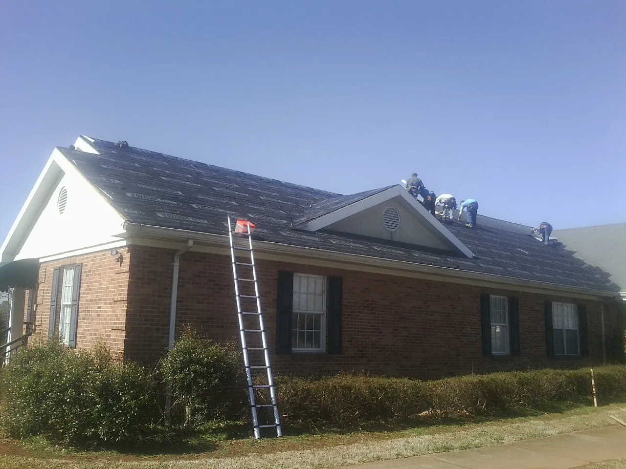 Crew tearing shingles off a brick ranch roof with a ladder set — Emergency Roof Repair work by our crew in Hammonton