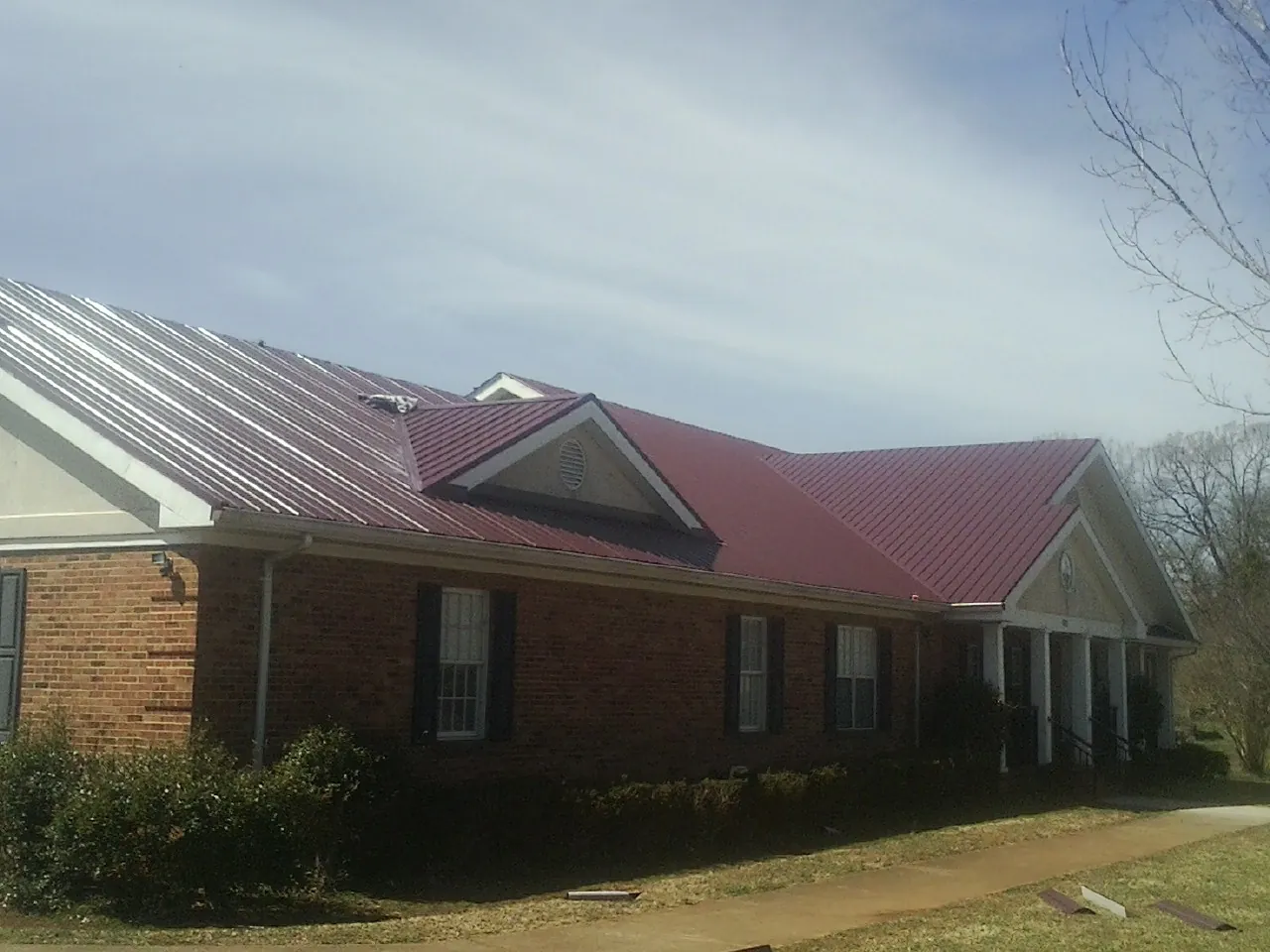 Red metal roof with gabled entries on a long brick building, from a Hail Damage Roof Repair job in Hammonton