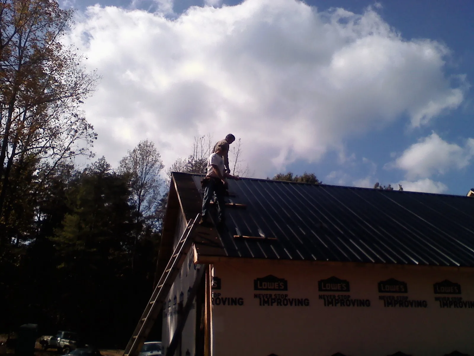 Roofer fastening dark metal panels high against a cloudy sky, from a Roof Inspection job in Hammonton