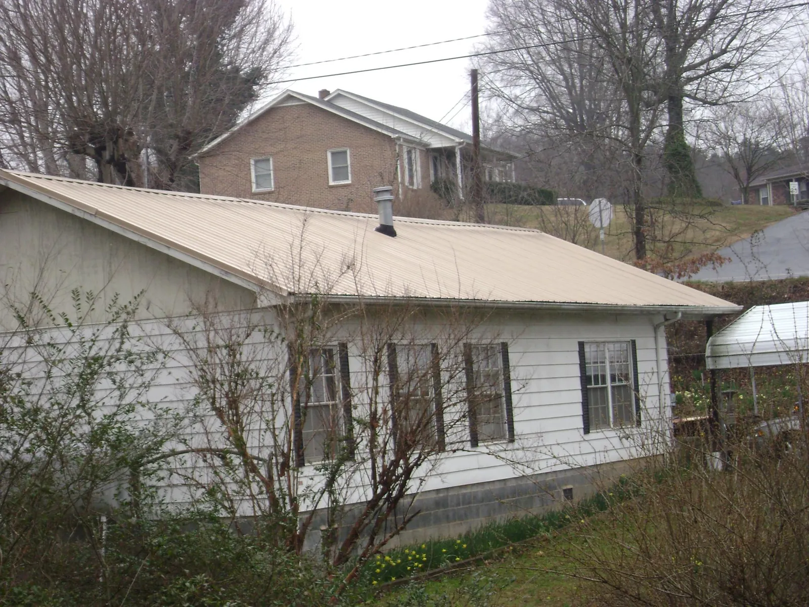 Tan metal roof on a white sided house set into a hillside — Commercial Roofing by Roofing Brothers in Hammonton